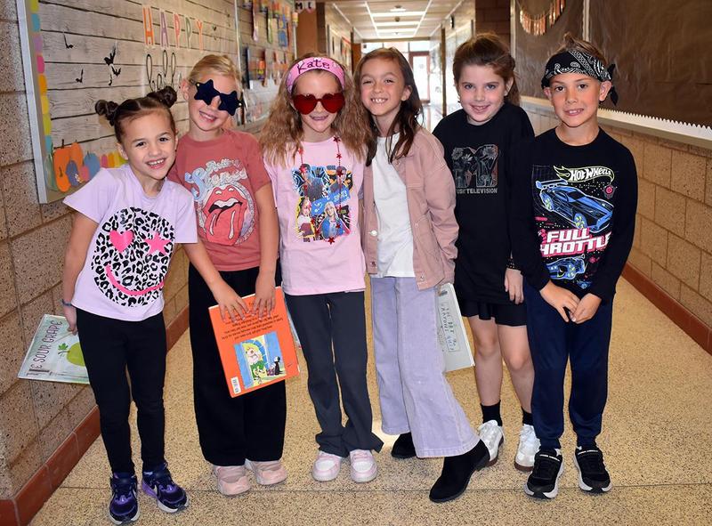 Six kids dressed in fun outfits pose together in a school hallway.