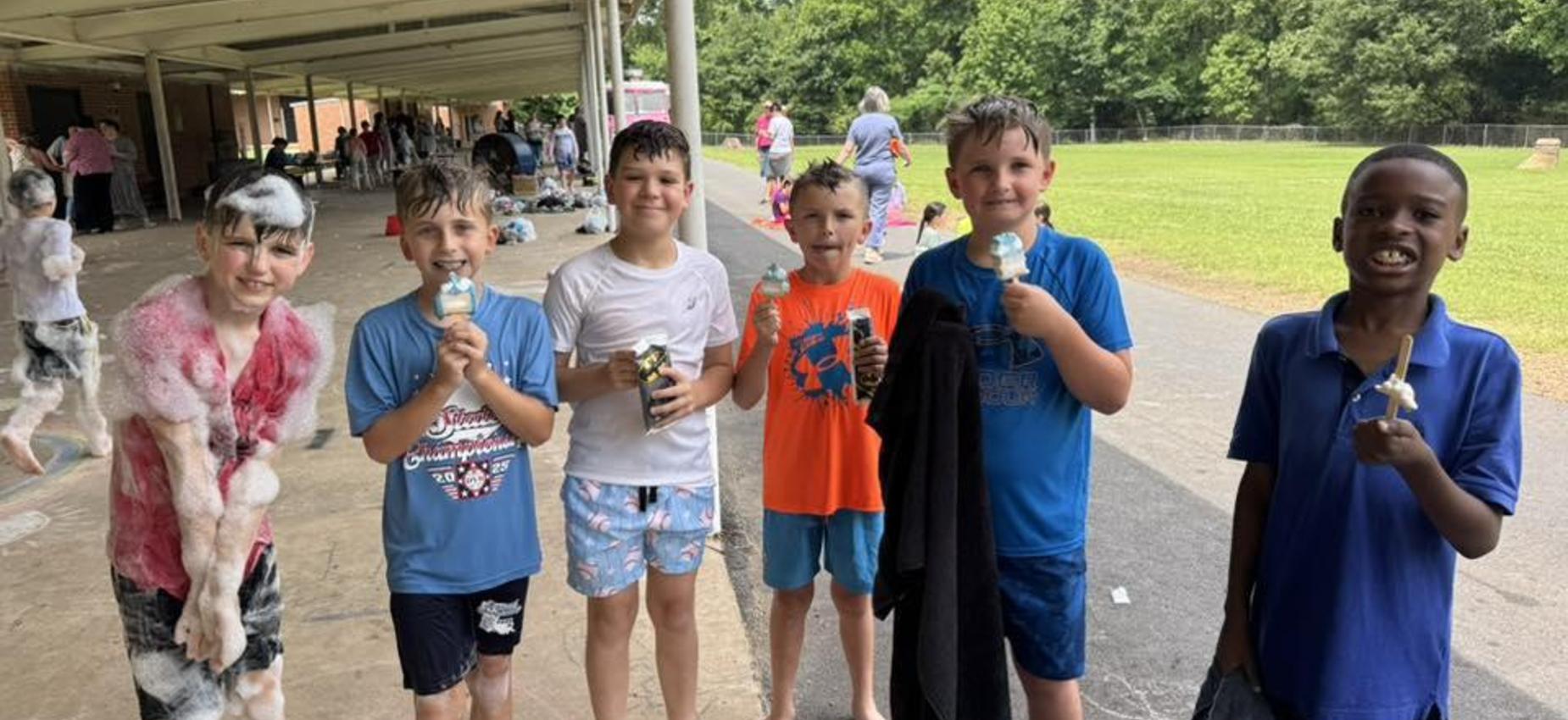 A group of six children enjoying ice cream after a water play event outdoors.