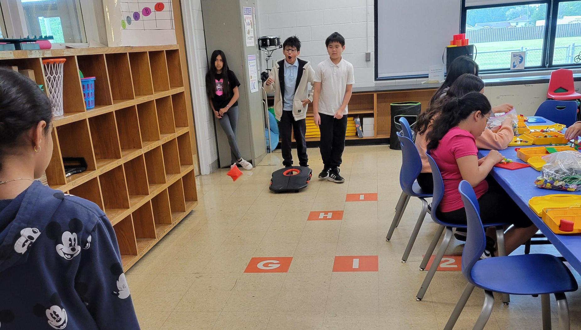 Children playing on a classroom floor with letters and mats.