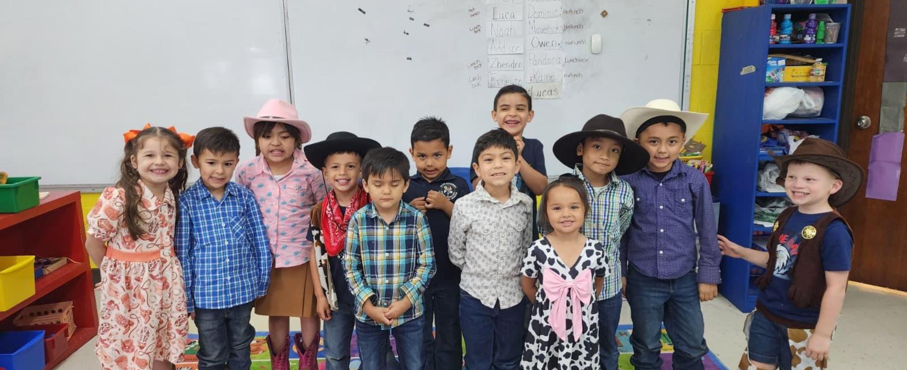 A group of children dressed in various outfits, smiling in a classroom setting.