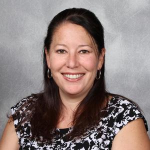 Jennifer Ambrose, a woman with shoulder length brown hair in a black and white floral blouse smiling