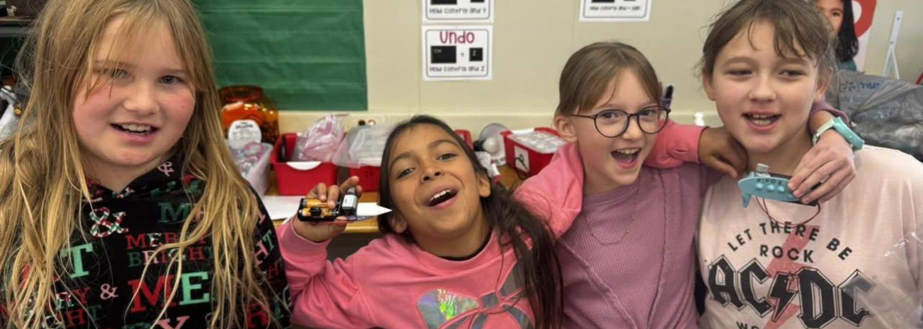 Four children laughing and posing with props in a classroom setting.