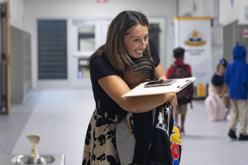 An elementary teacher smiles and gives a hug to a student