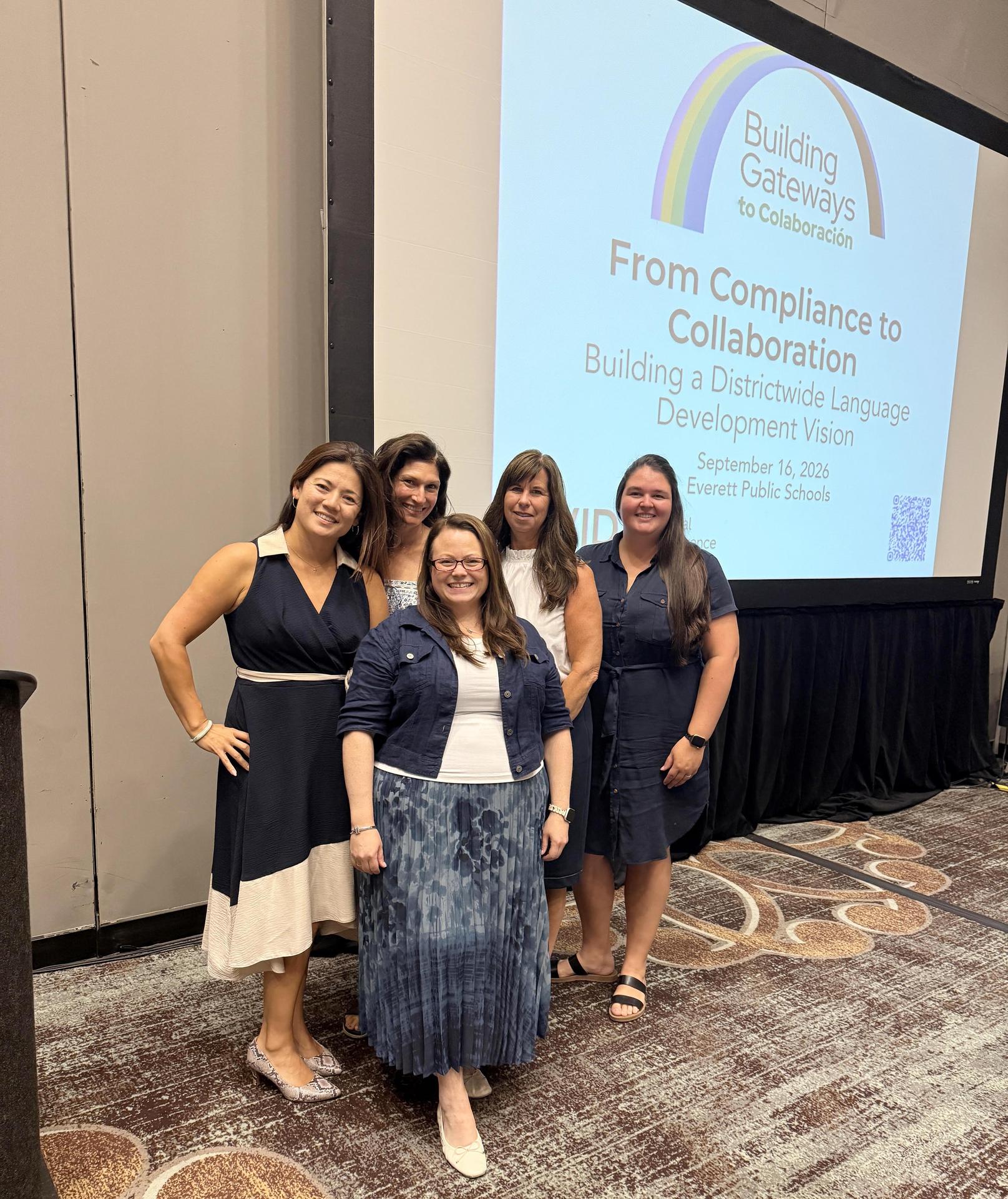 Five women standing in front of a large screen at a conference