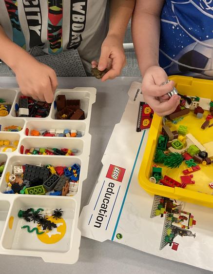 Two children building with colorful LEGO pieces on a table.