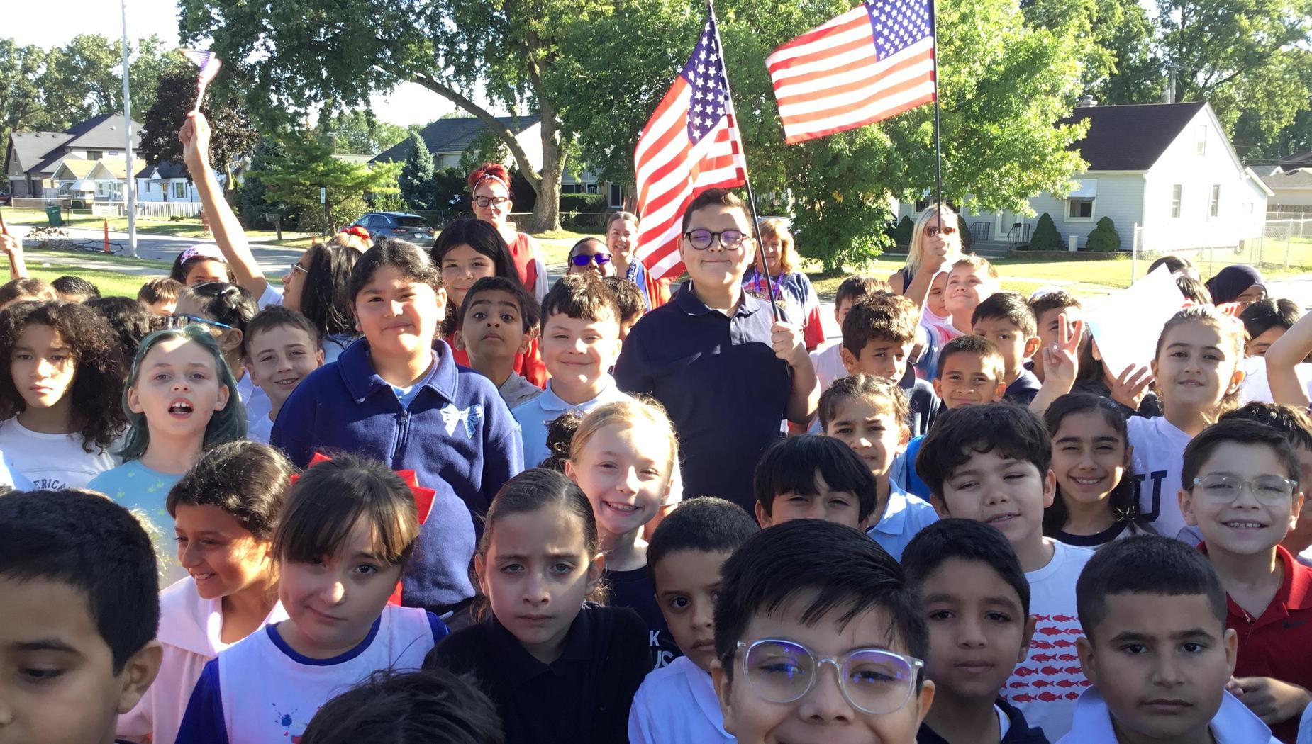 A group of children smiling, holding flags and celebrating outdoors.
