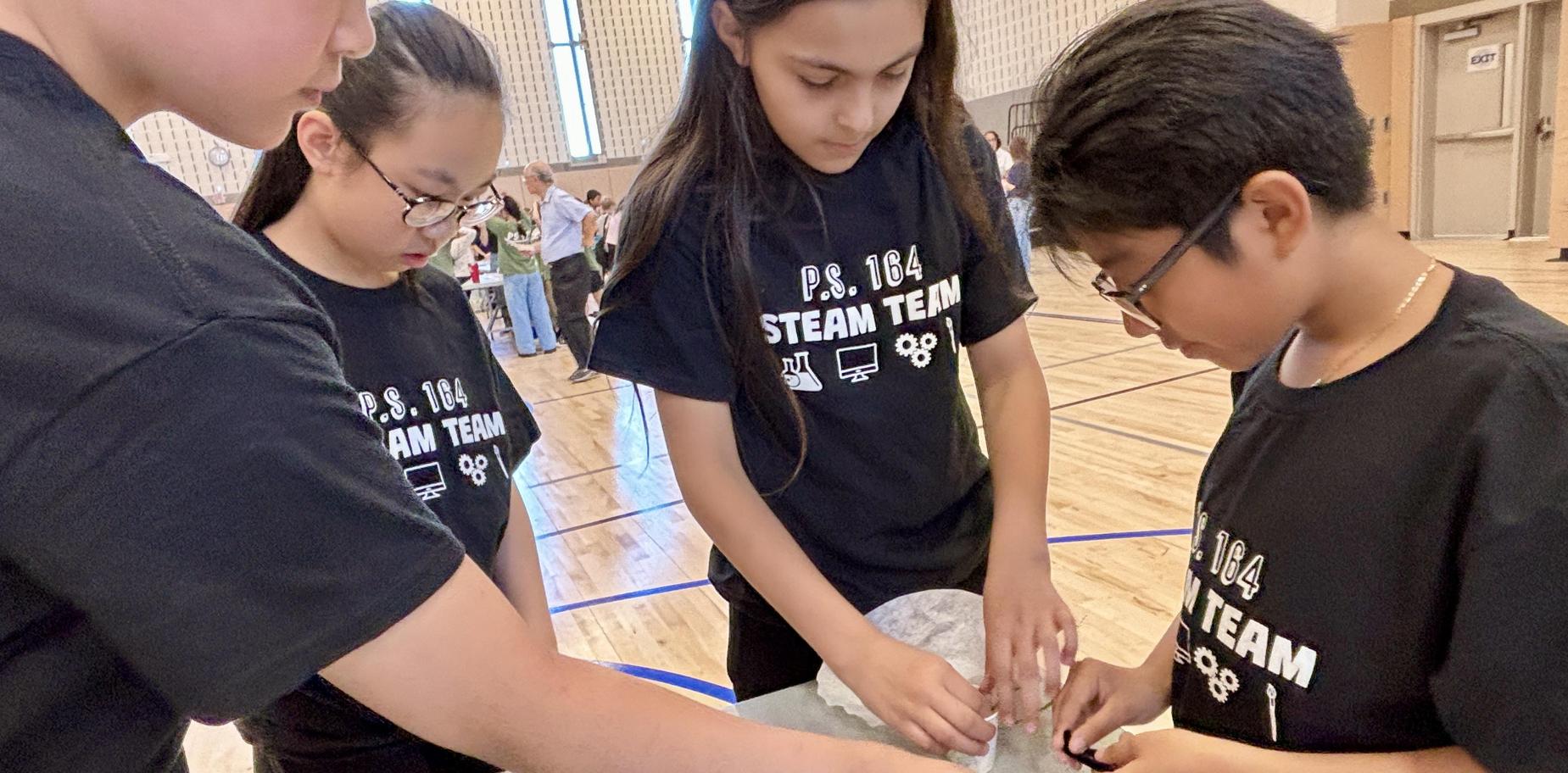 Four students in matching shirts collaborate on a project at a school event.
