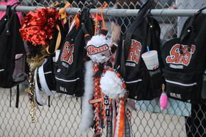 Cheerleading accessories and backpacks hang on a fence at the game.