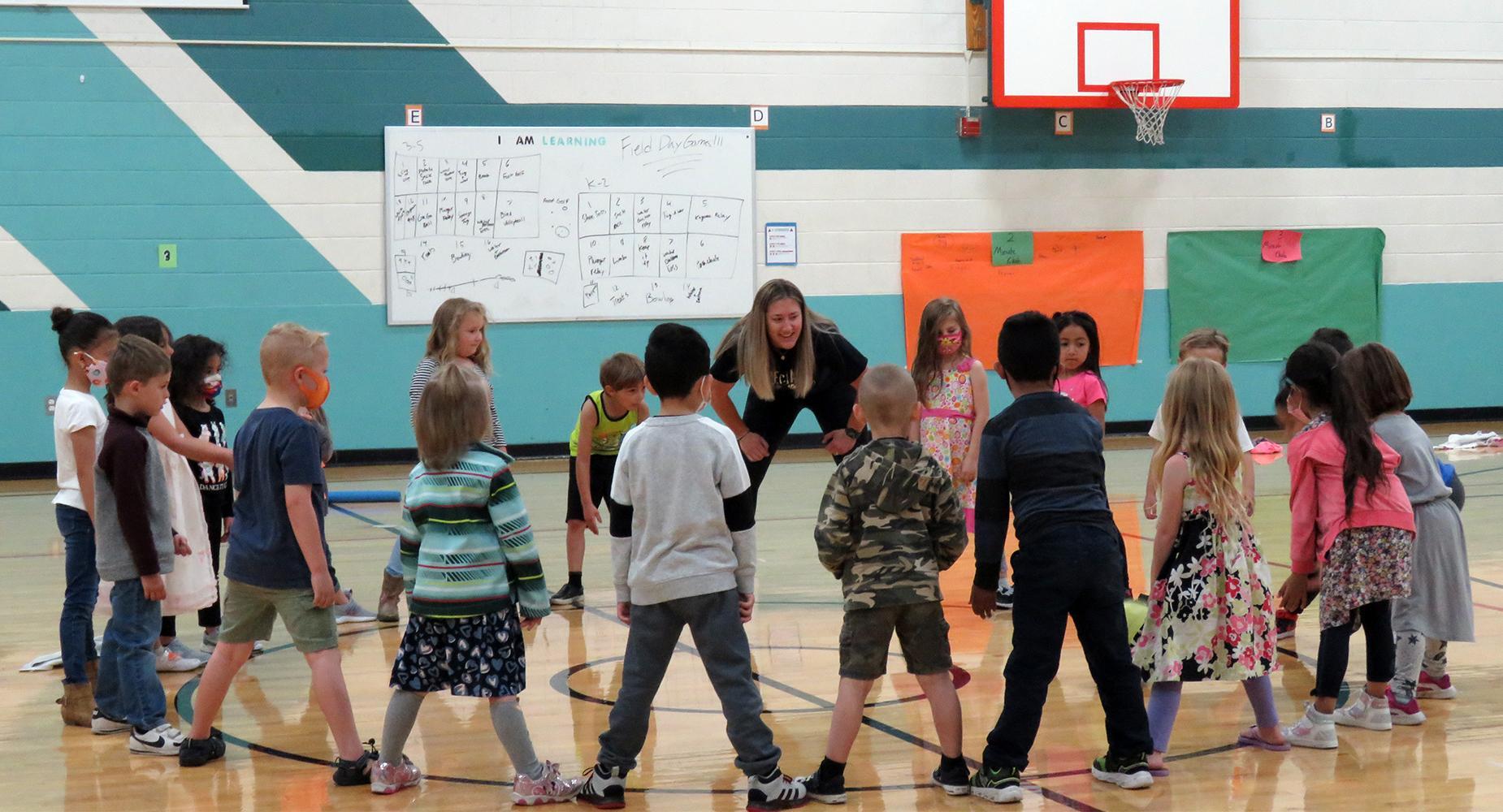 Young children in a circle with PE teacher, passing a ball
