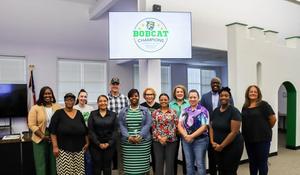 Group of people standing in front of a screen displaying 'Bobcat Champions' logo.