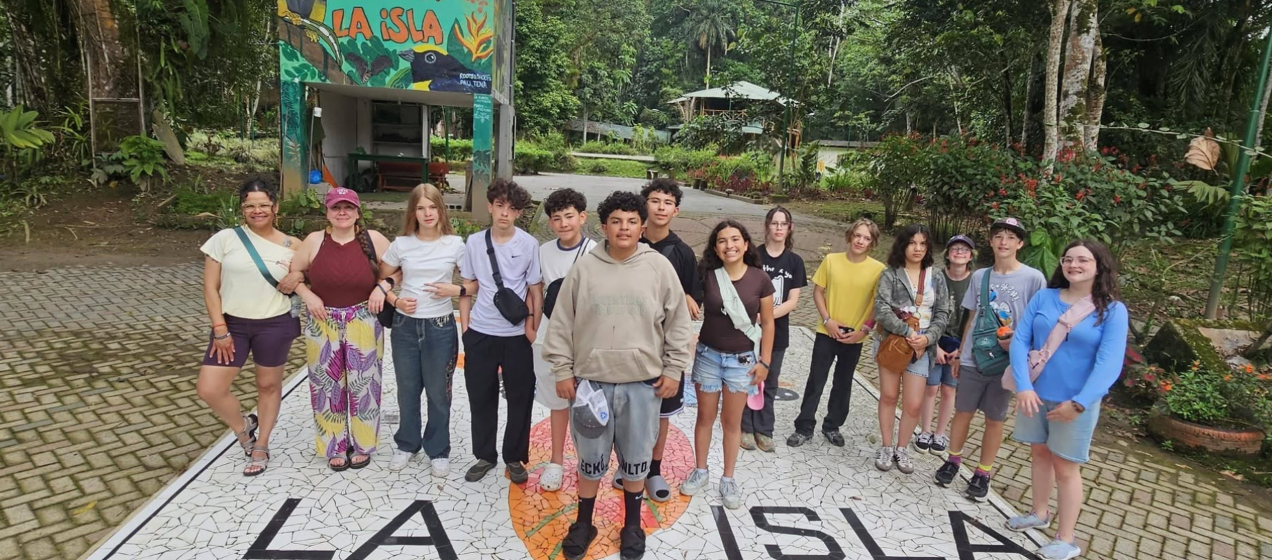 Group of people standing in front of a sign that reads 'LA ISLA' in a tropical setting.