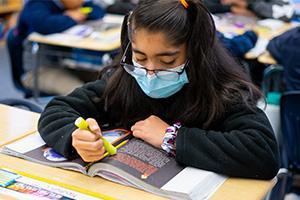 Student wearing a facemask reading a textbook