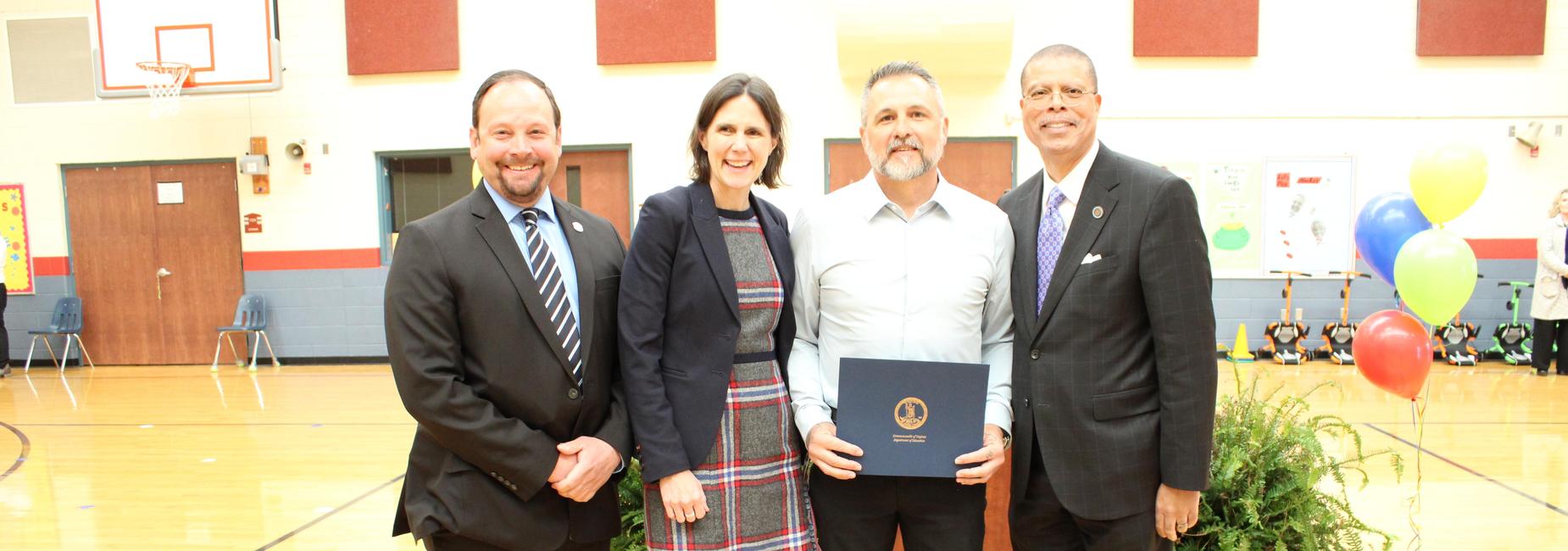 four adults posing for picture in front of podium in a gym