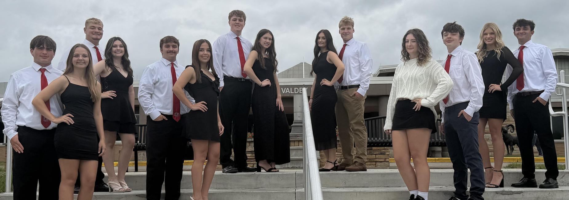 Group of teenagers in formal attire posing on stairs outside a building.