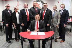 Dr. Teddy Clevenger signing contract with school board members standing behind him