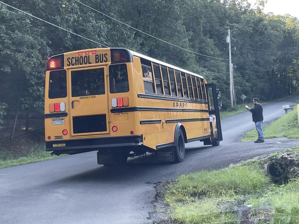 A man standing outside putting his child on the school bus.