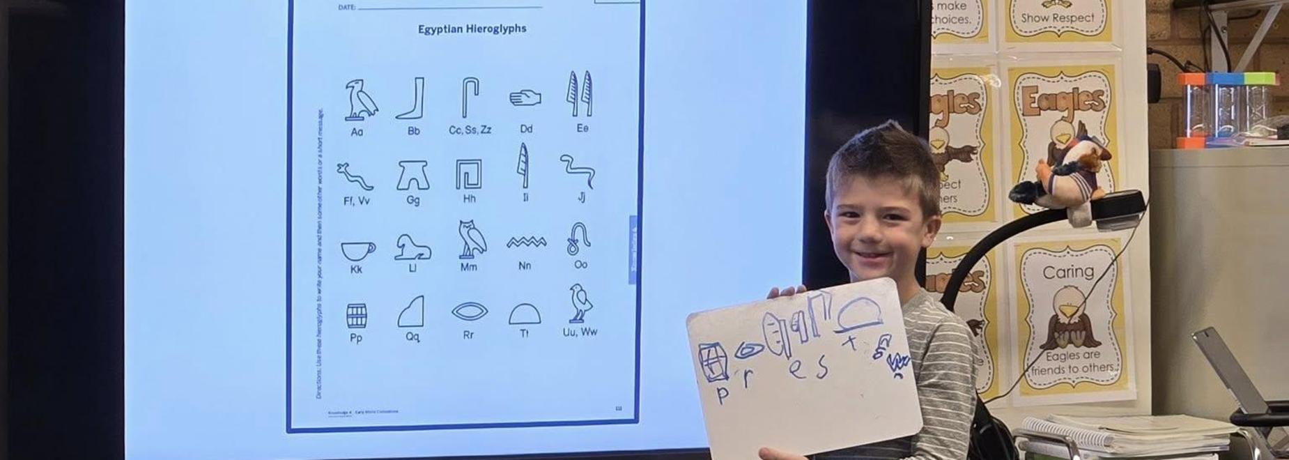 Child presenting Egyptian hieroglyphs with a whiteboard in a classroom setting.