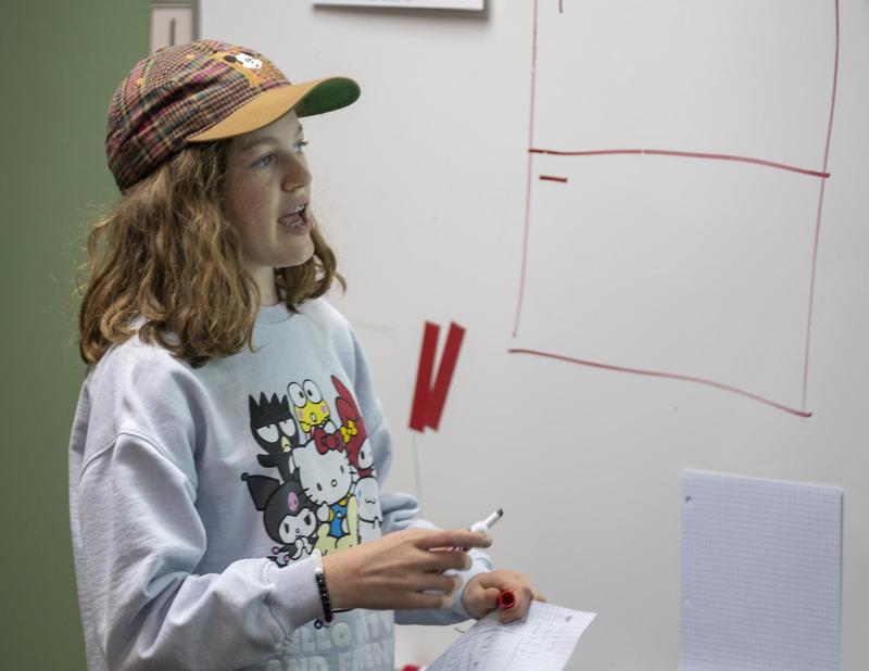 Student in hat at white board explaining math concepts.