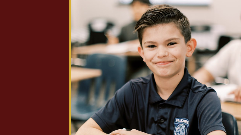 A smiling student in uniform sits in a classroom