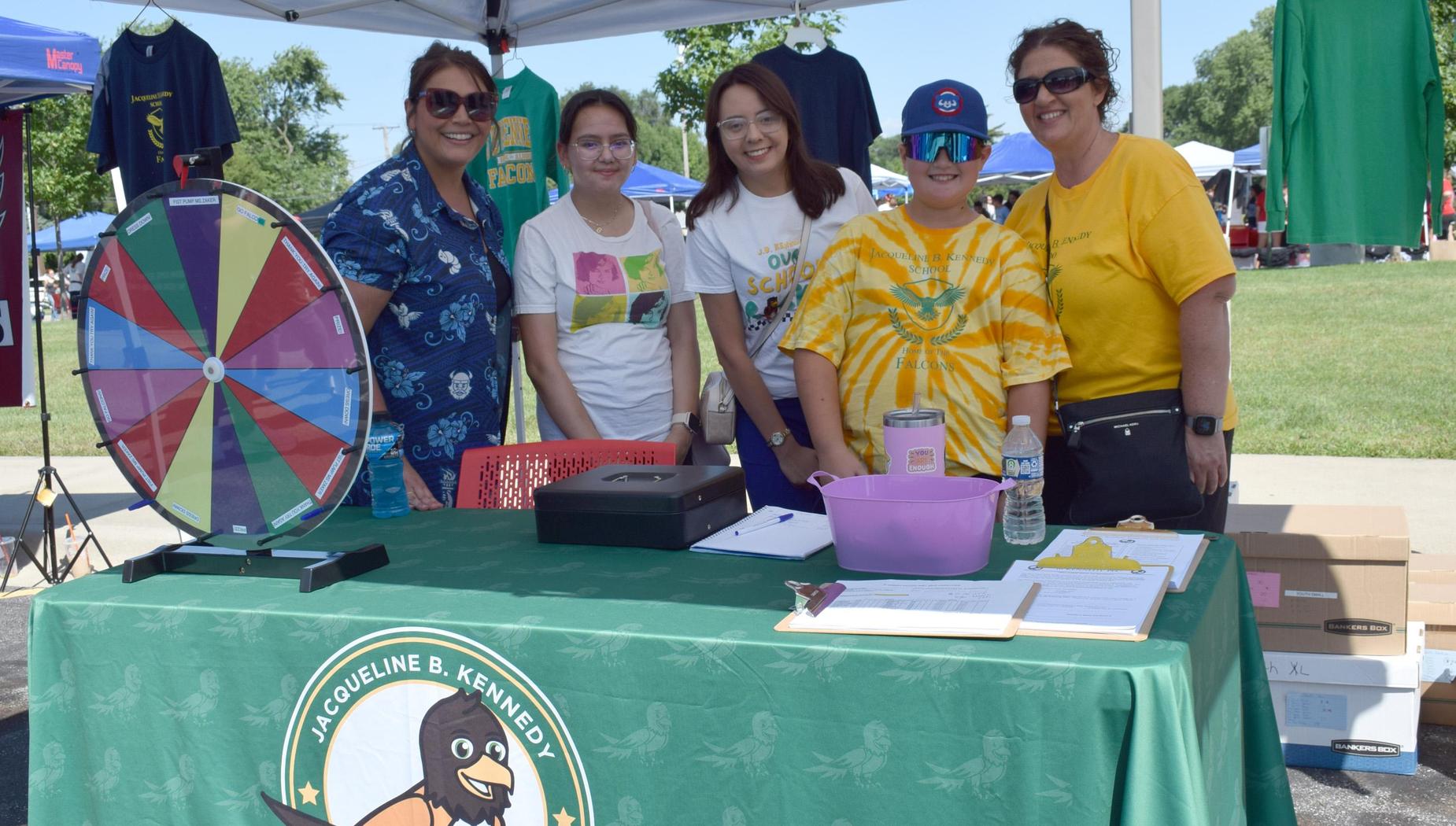 A group of people at a table with a game wheel and a green tablecloth at an event.