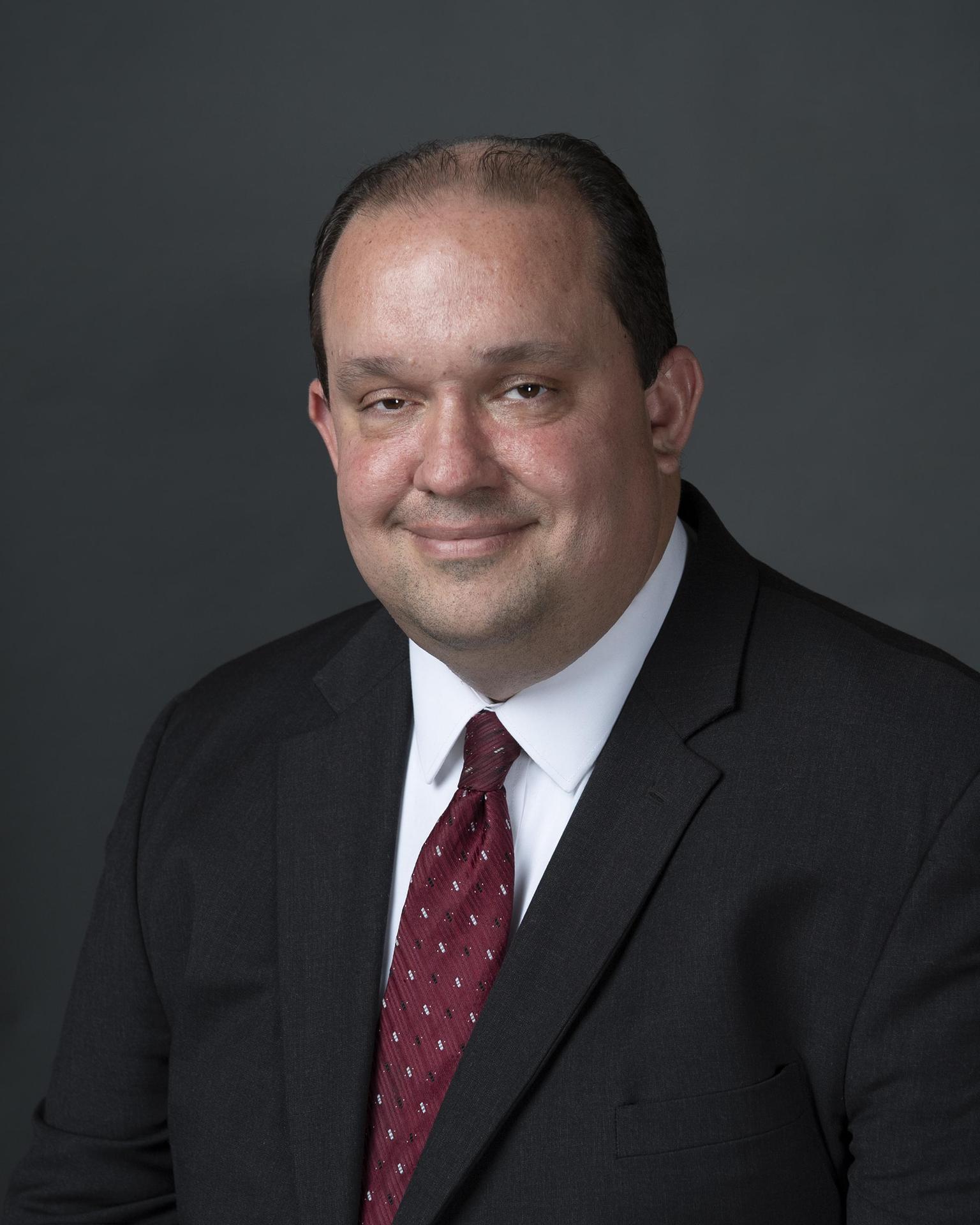 Portait of a man posing in a suit and dark red tie.