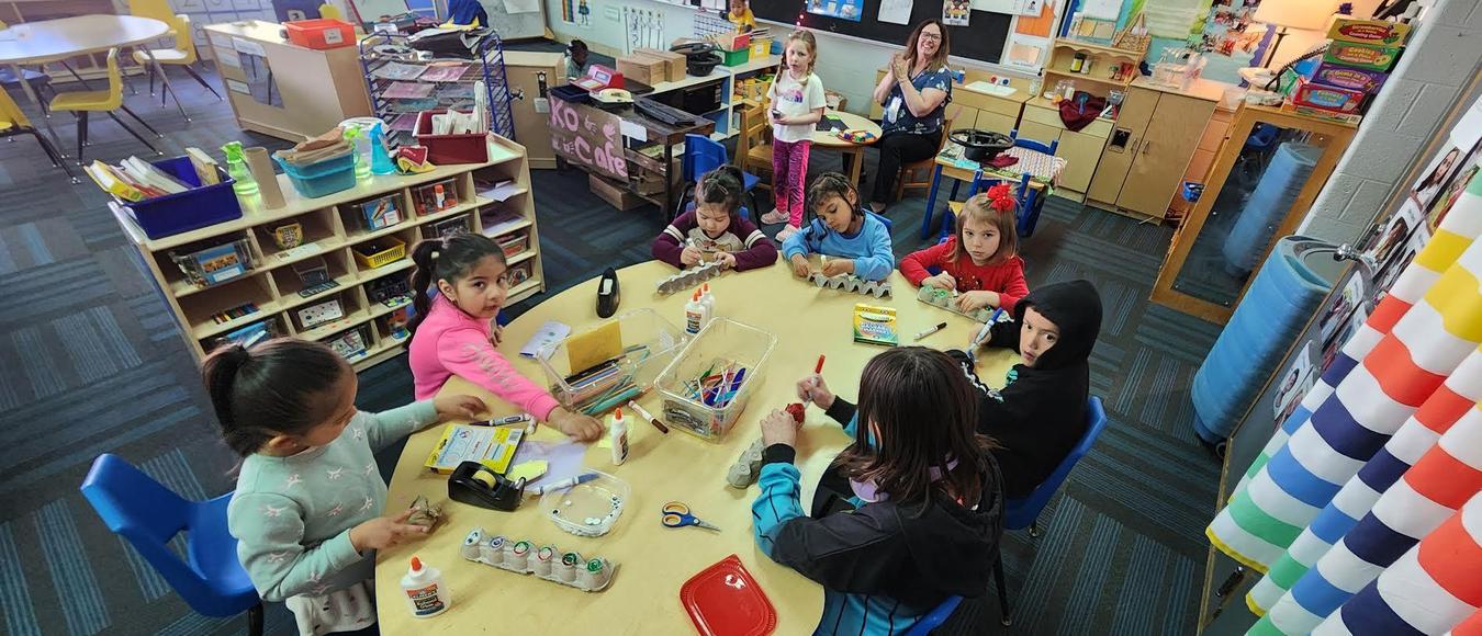 Children are sitting at a table doing some arts and crafts.