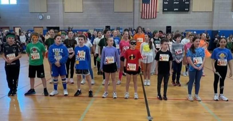 Groups of children in colorful clothing lined up for an event in a school gym.