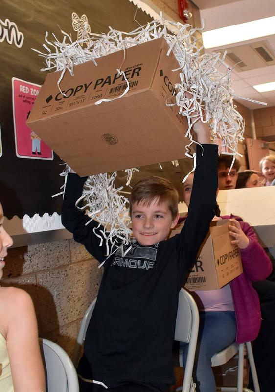 A boy joyfully lifts a box overflowing with shredded paper above his head.