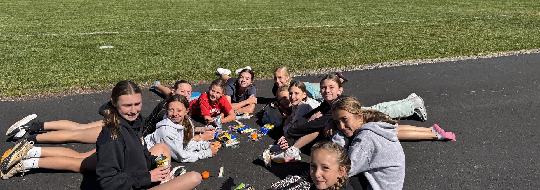 A group of girls sitting on the ground, enjoying snacks on a sunny day.