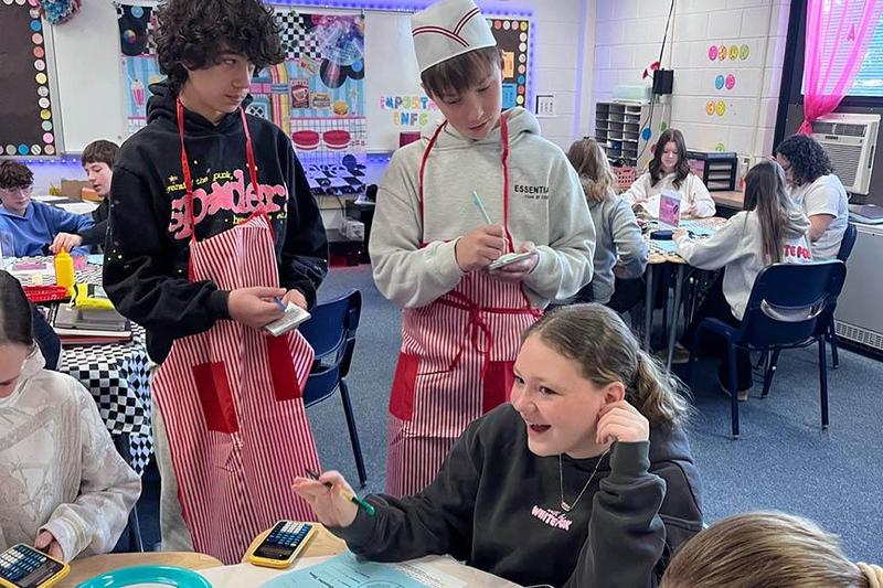 a student gives her order to two other students who hold notepads and wear aprons