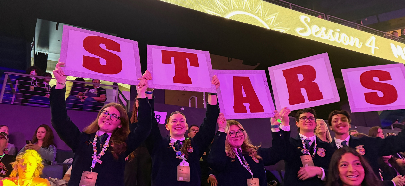 Students enthusiastically holding signs that spell 'STARS' at a lively event.