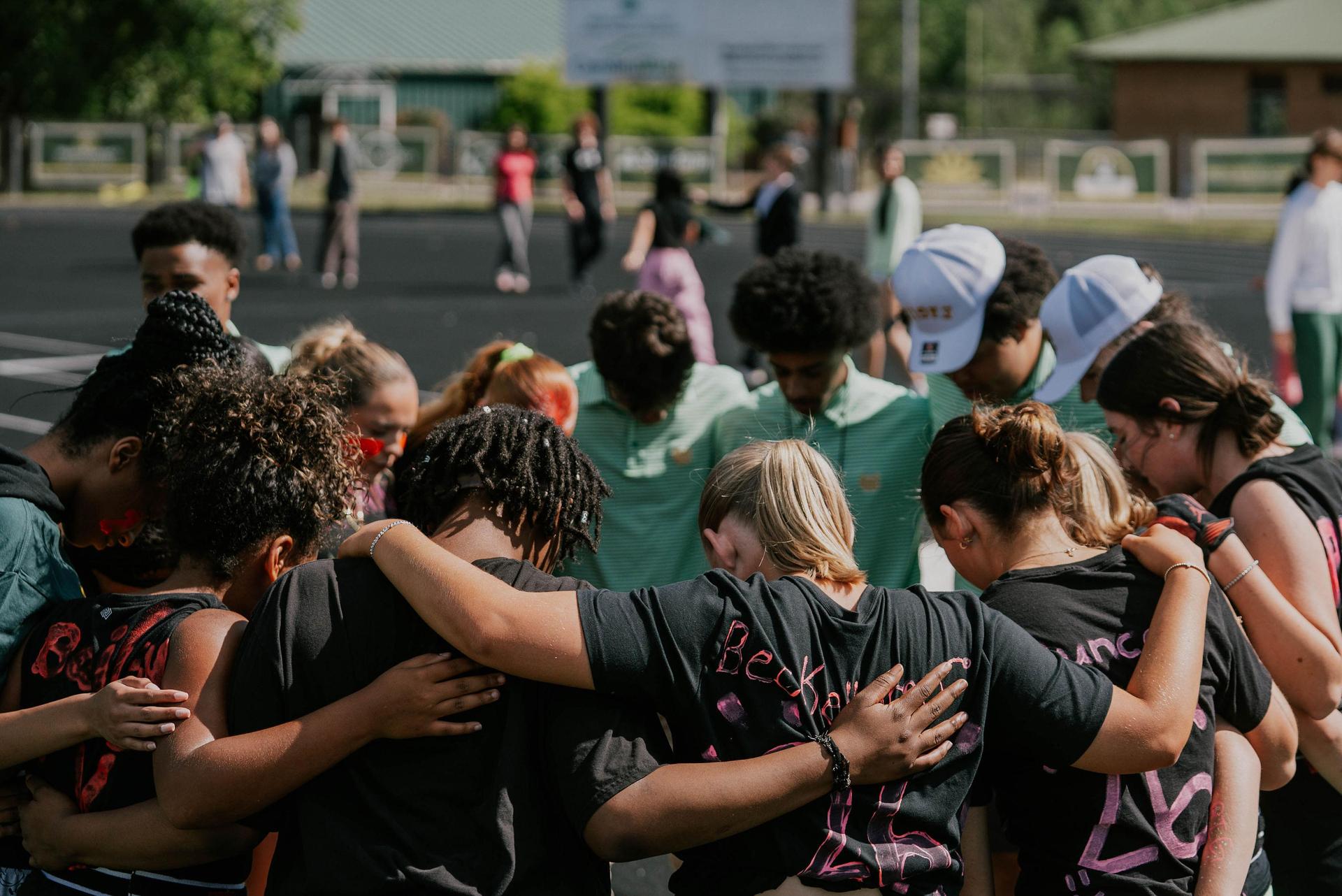 A group of teenagers huddled together in a moment of unity on a sports field.