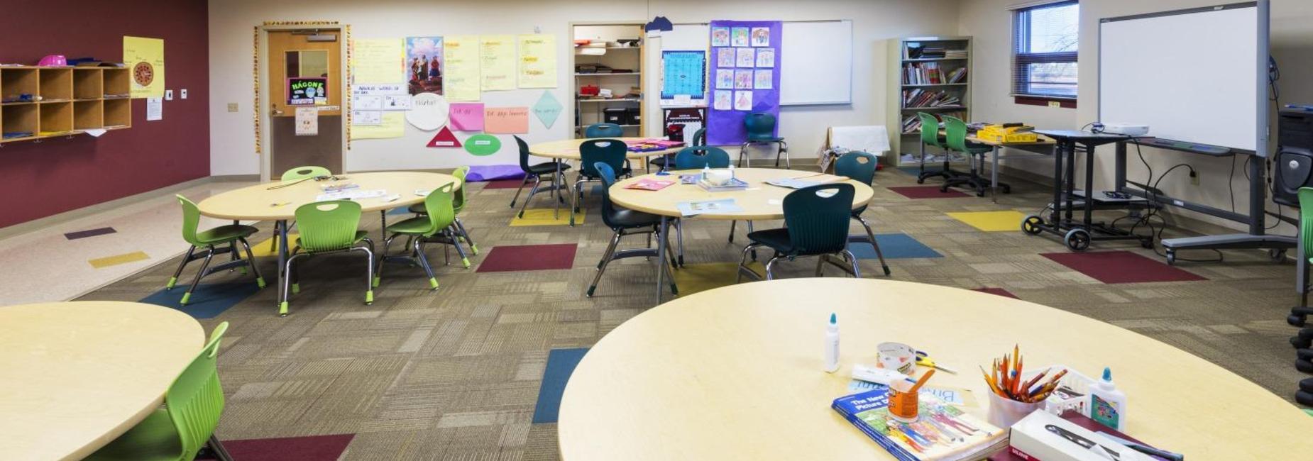 A classroom with circular tables, green chairs, and educational materials displayed.