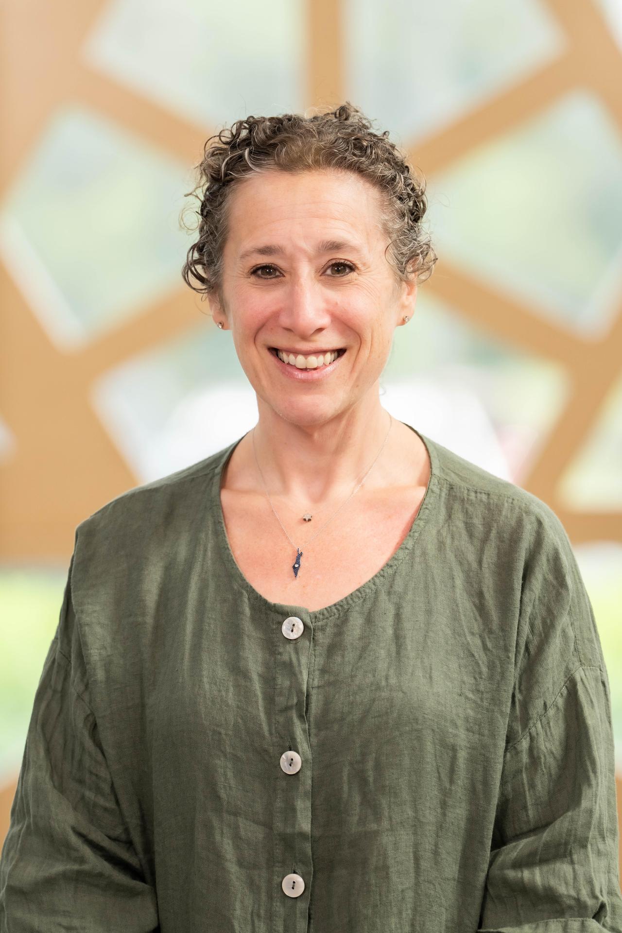Ali Tannenbaum wearing a green shirt, curly hair pulled back, smiling