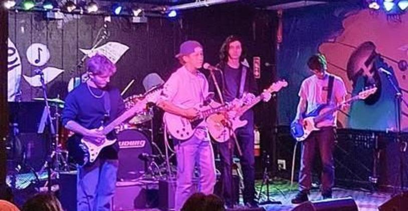 Four musicians performing on stage with guitars and drums in a vibrant venue.