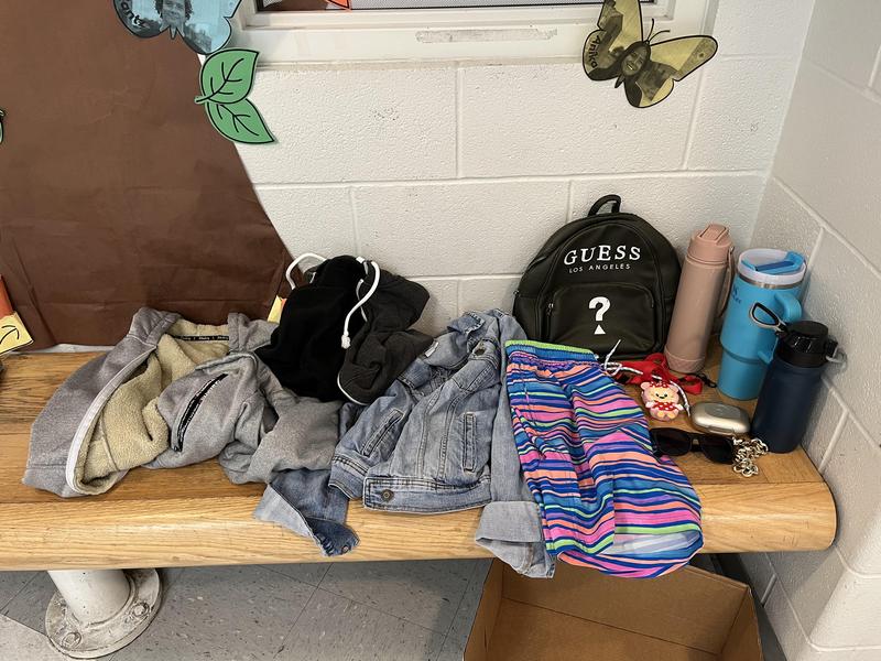 Lost and Found items: gray jacket, black/dark gray jacket, denim jacket, stripped colorful shorts, Guess backpack, pink water bottle, blue stanley cup, navy blue water bottle, red lanyard, minnie mouse case, silver metal case, black sunglasses.