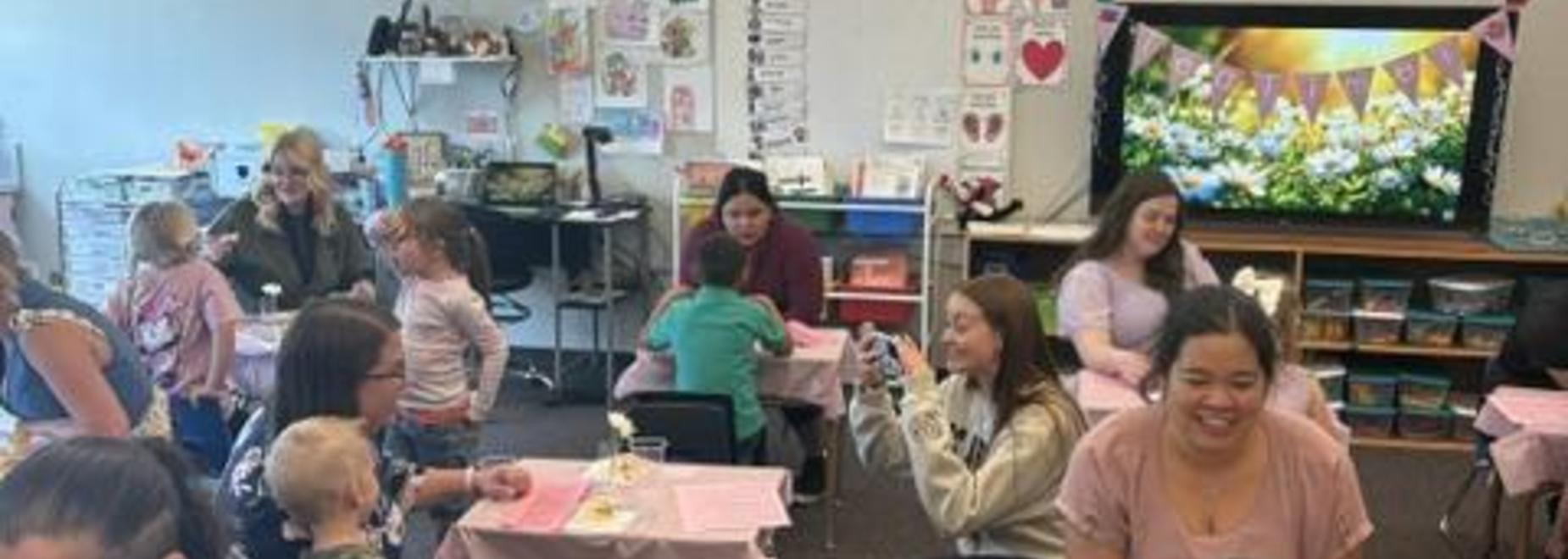 Classroom scene with adults and children enjoying activities at tables.