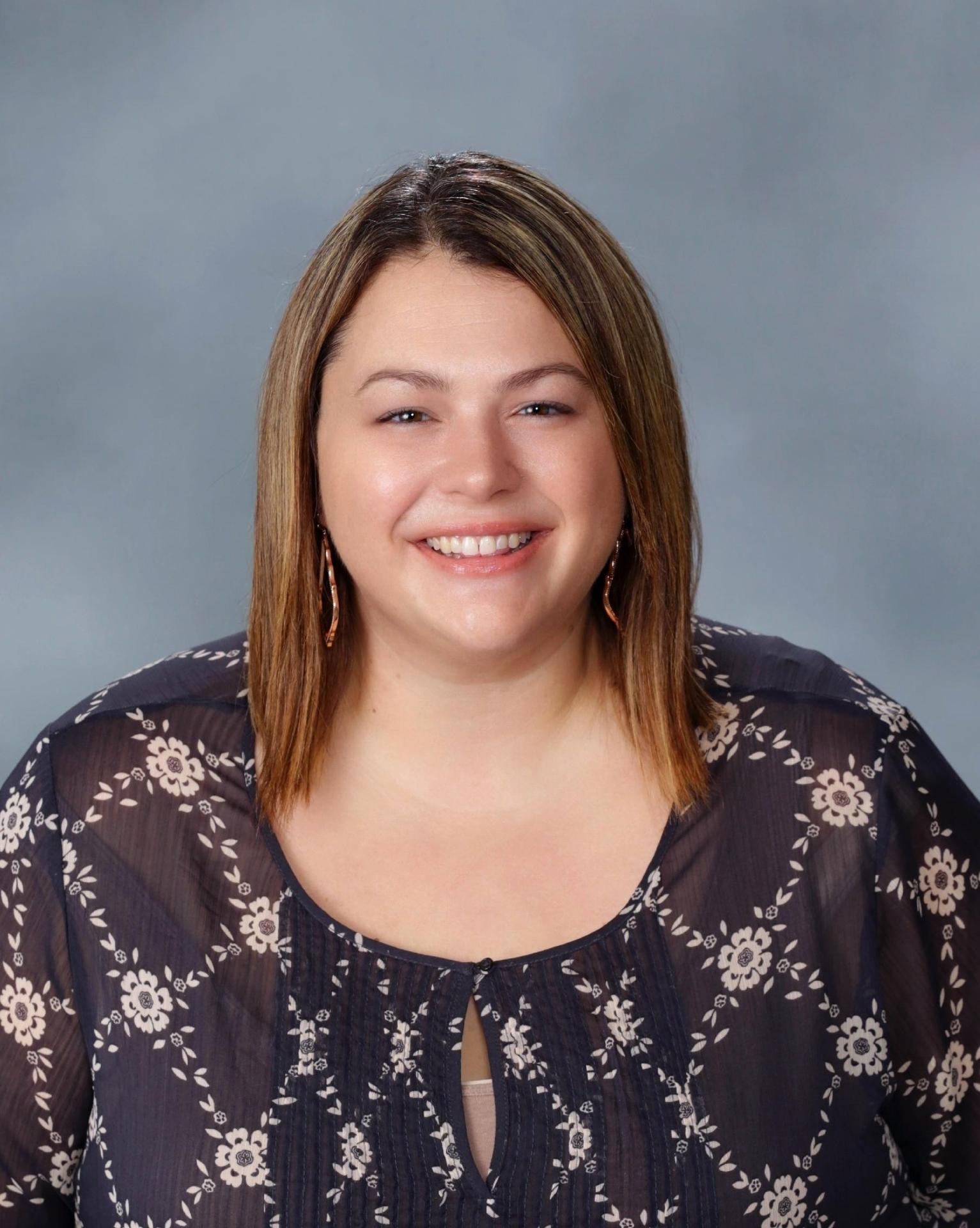 Smiling woman with brown hair in a dark floral top against a gray background.
