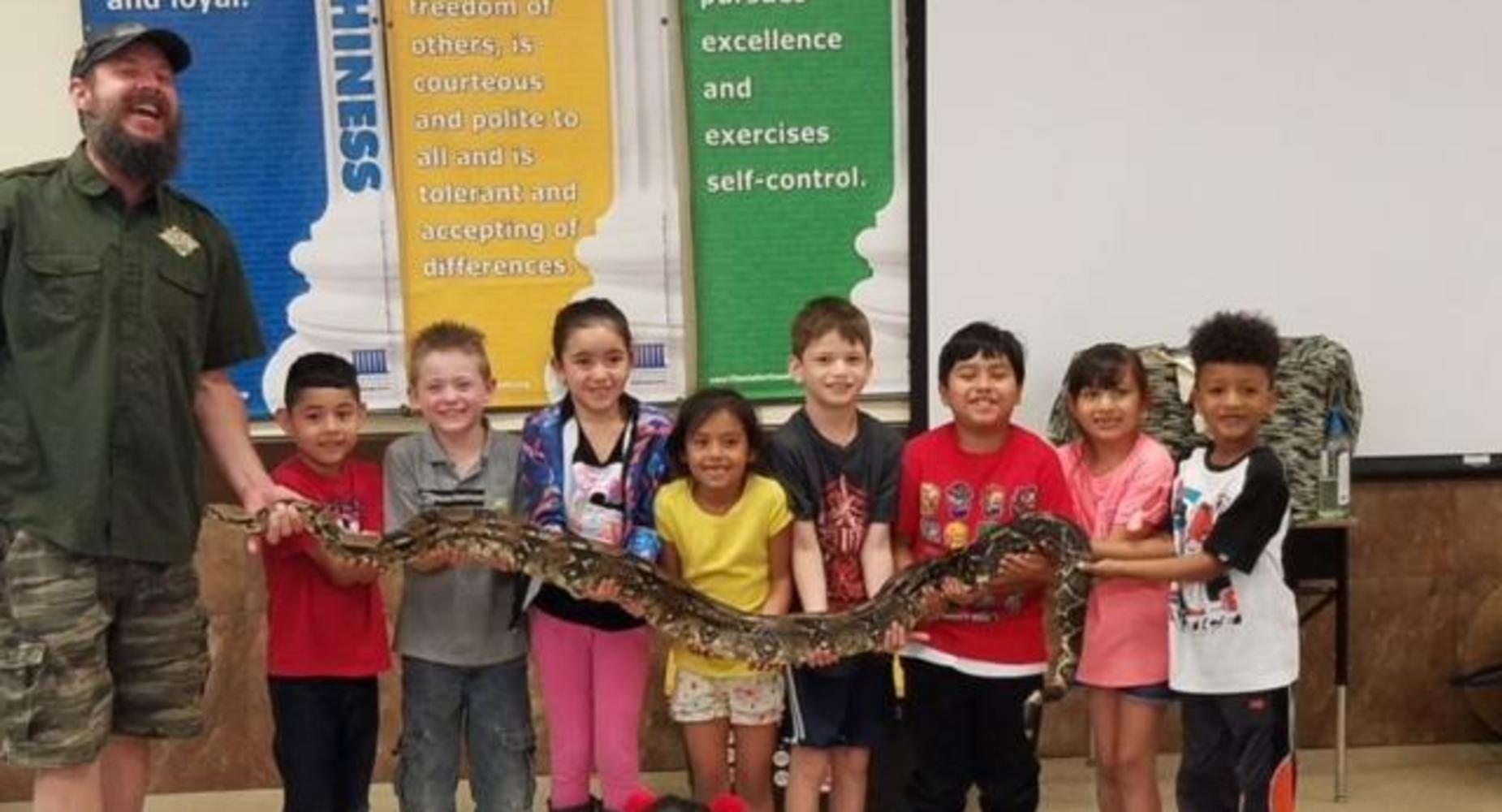 Cypress students holding a large snake at a school assembly with the help of a trained professional