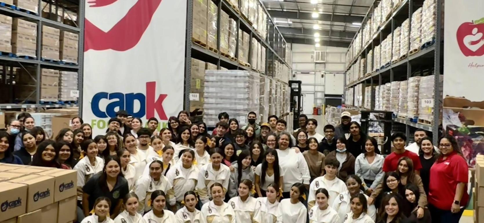 A large group of people poses together in a warehouse filled with stacked boxes.