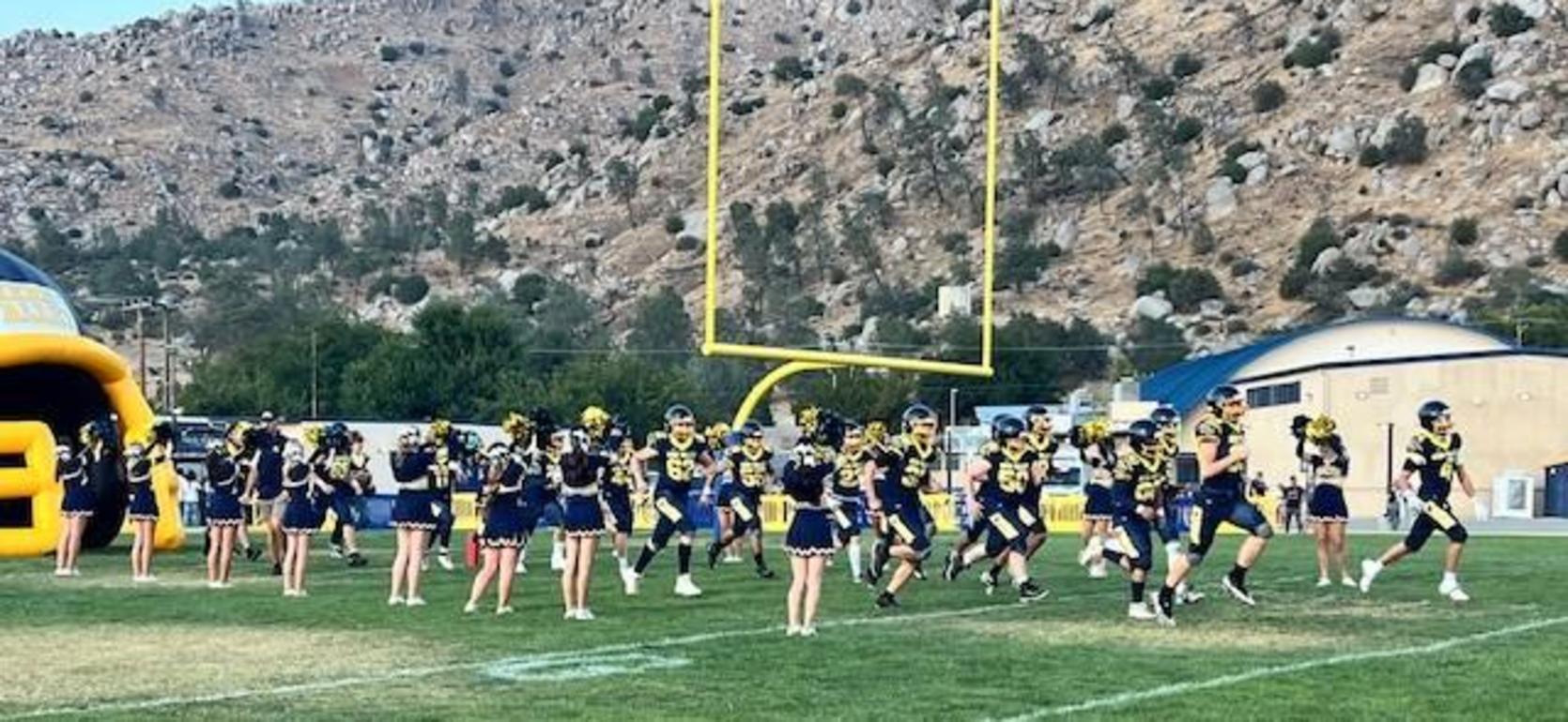 Cheerleaders performing in front of a football team and mountains.
