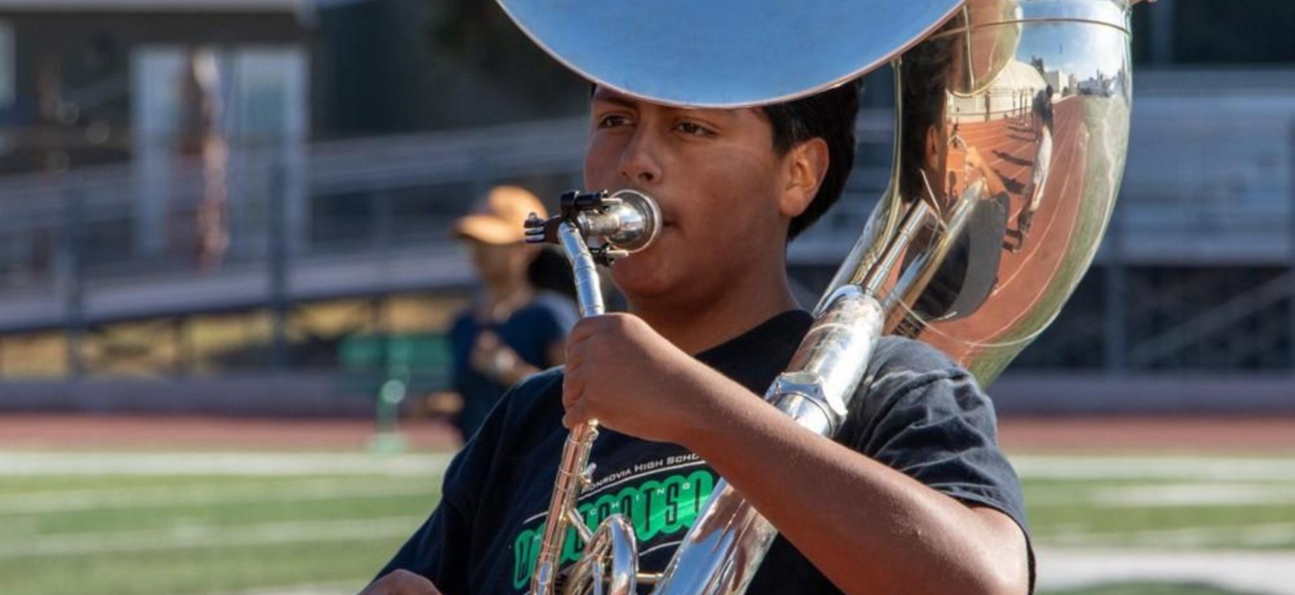 Young musician playing a tuba in a marching band on a field.