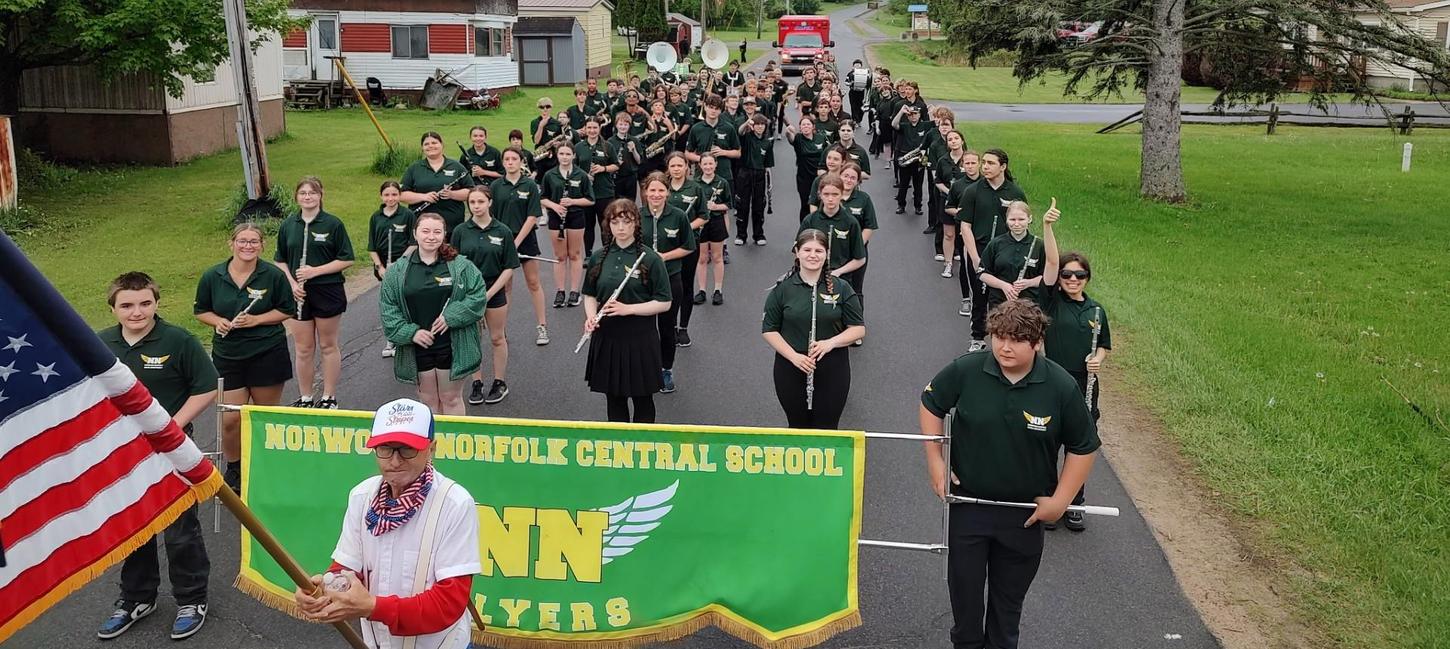 Marching band stands outside with the NNCS banner in front of them