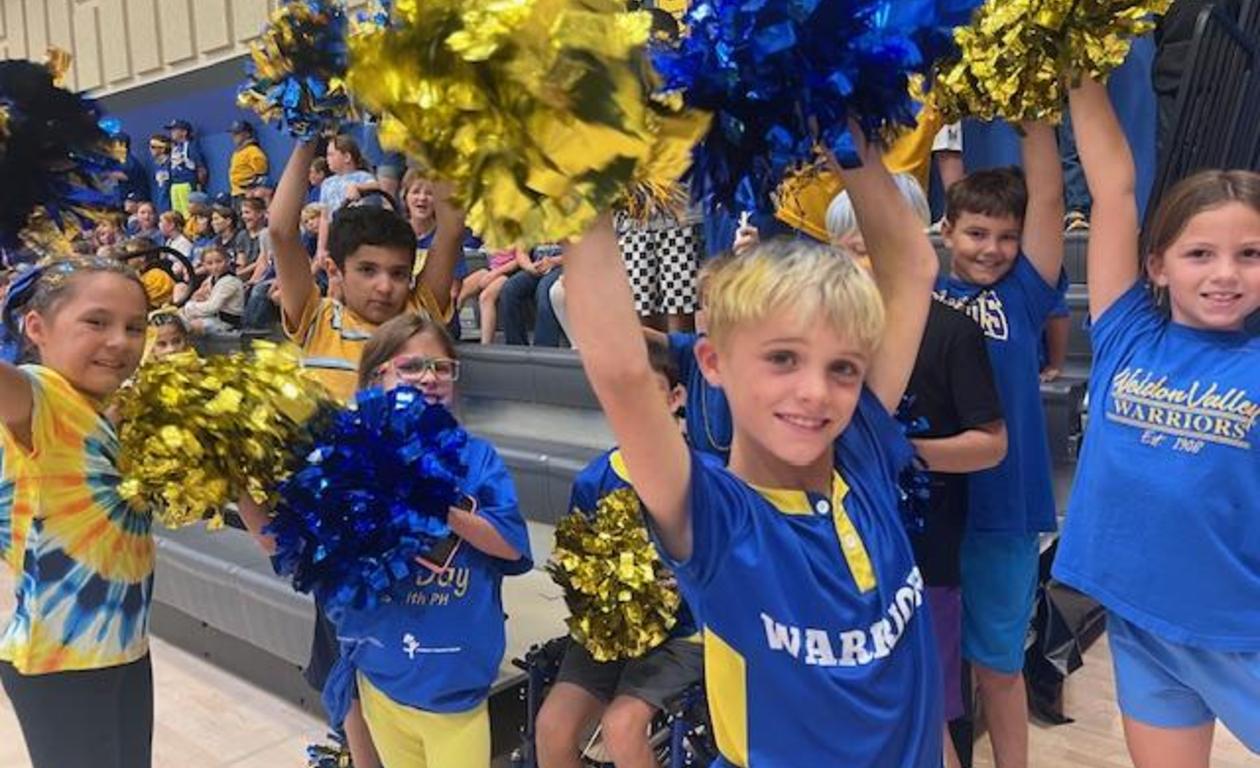 Cheerful children holding blue and gold pom-poms, excitedly posing in the gym.
