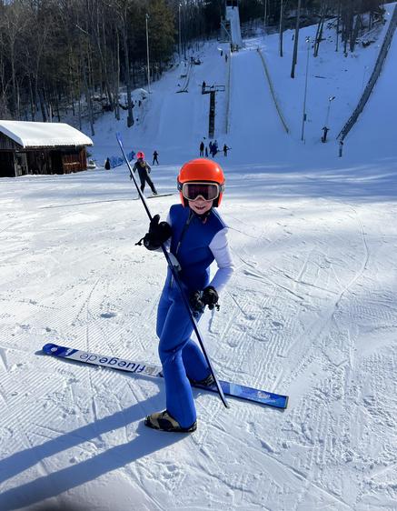 Girl in ski suit poses with skis, wearing a helmet and goggles.