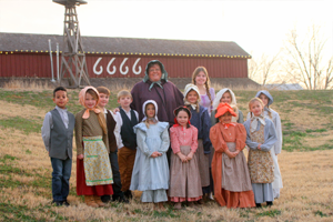 Saundra posing with a group of 1st graders who are doing a reenactment at a 19th-century one-room schoolhouse at the National Ranching Heritage Center