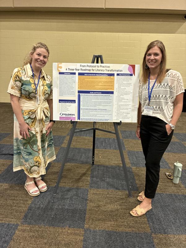 two adult women stand on either side of a poster about literacy