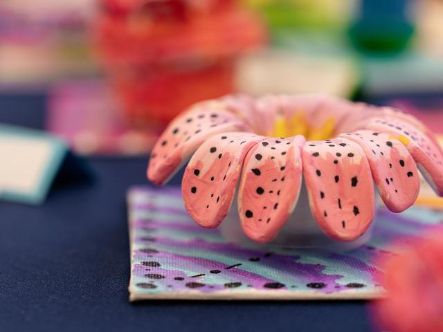 Colorful clay flower with pink petals and black speckles on a patterned background.