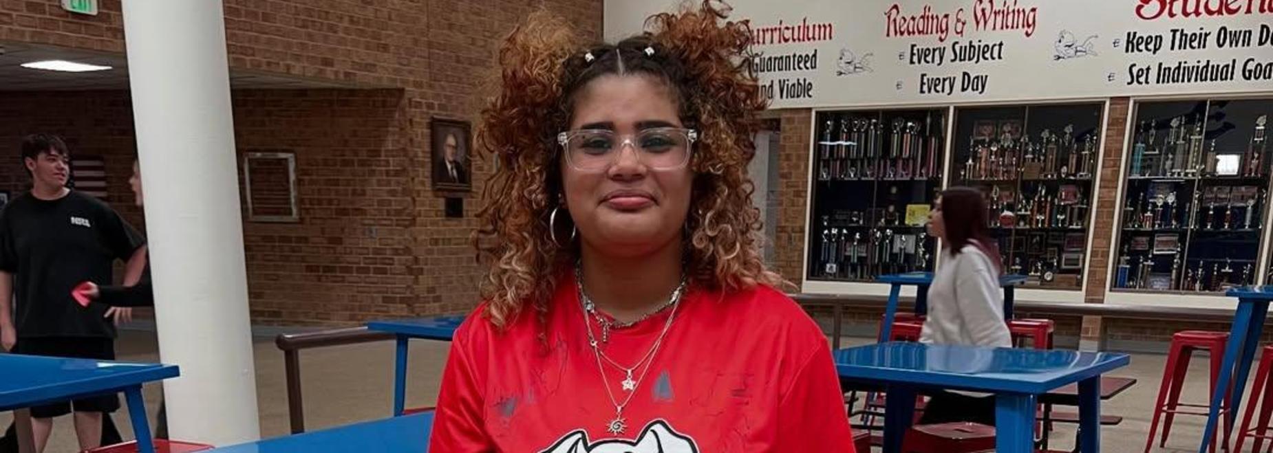 Student wearing a red shirt with a cartoon dog design in a cafeteria setting.