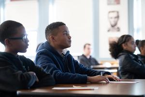 Promise students sit at their desks with light pouring in from the windows behind them